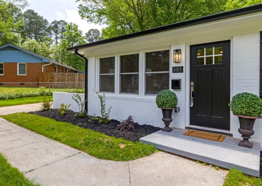 White brick ranch house with black front door, potted shrubs in urns and fresh mulch beds