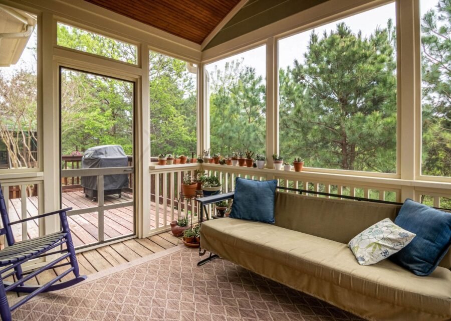 Screened porch with a daybed sofa, blue pillows, a rocking chair and a grill on the deck outside